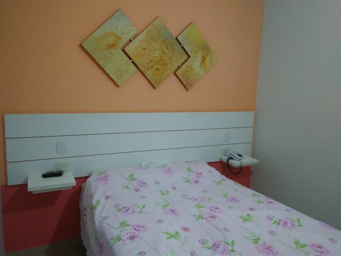 Quarto de casal com parede salmão, cabeceira branca e quadros em losango