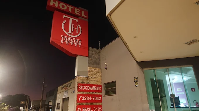 Letreiro do Trevise Hotel aceso à noite com placa de estacionamento