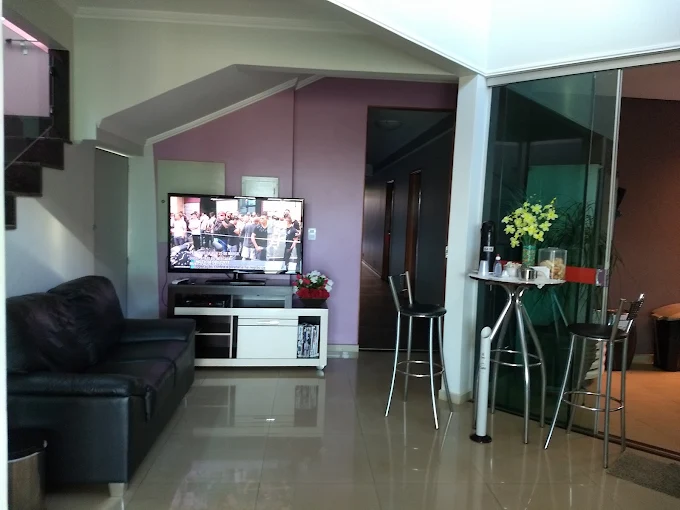 Sala de estar com sofá preto, TV e mesa alta com banquetas